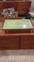 Vintage Cornell warming tray placed on wooden furniture, showing avocado green top with central decorative design and wood handles and legs.