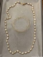 Full view of the necklace showing natural pearls and the gold clasp on a gray velvet surface.