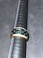 Close-up photo of gold plated ring showing dark blue rectangular stones and clear accent stones.