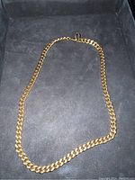 Full view of gold-tone curb chain necklace laid flat on dark surface