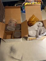 Two open boxes of drink glasses on a table, one with frosted holiday-themed glasses and one with amber glasses wrapped for protection.