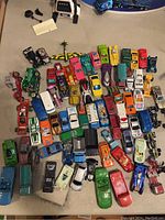 Overview of about 50 assorted vintage Hot Wheels and other toy cars and trucks spread on floor, paint wear and rough use visible