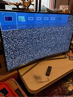 Front view of curved TV powered on showing static and menu options; remote control on table