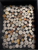 Full view of a tray with numerous foreign coins arranged, various metals and sizes visible, including two coins mounted in gold-colored keychain holders.