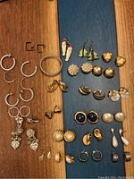 Top view of assorted custom earrings showing variety in style, size, and color on wood and blue background.