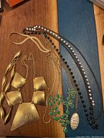 Custom jewelry pieces on wooden surface including gold-tone textured necklace and bracelet, beaded necklaces, and green stone floral necklace.