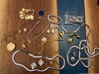 Top-down view of assorted custom jewelry pieces spread out on a wooden surface including bracelets, chains, pendants, pins, and earrings