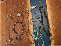 Full overview of the jewelry lot on wood table with various necklaces, bracelets, earrings, and brooches arranged
