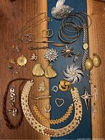 Full view of assorted custom jewelry items laid out on wooden surface including necklaces, earrings, brooches, bracelets, and a bag of metal charms.