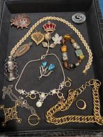 Various pieces of custom jewelry including necklaces, brooches, a bracelet, and a ring laid out in a black tray.