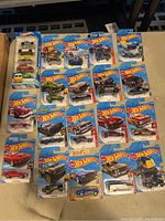 Full view of the 19 Hot Wheels cars in original packaging arranged on a surface, showing varied models and colorful cards.