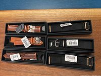 Six Daniel Wellington watch straps in original boxes on wood surface, three brown leather and three black nylon