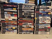 Wide overhead shot showing stacked game cases with visible titles for many PlayStation 2 games, focusing on sports and racing video games.