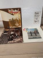 Four vinyl records displayed upright and flat showing album covers of Led Zeppelin II, Pink Floyd The Wall, The Who Meaty Beaty Big and Bouncy, and one additional record.