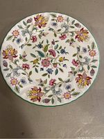 Top view of a vintage Minton Haddon Hall bone china plate with colorful floral designs and green rim.
