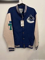 Front view of varsity-style sweatshirt with blue body, beige sleeves, Canucks logo patch on front left chest, and number 70 on right sleeve.