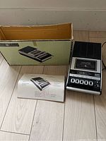 Cassette tape player with original box and instruction manual on floor.
