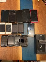 Lot of 13 used phones of various brands including Samsung, Apple iPhone, BlackBerry, and LG on wooden surface.