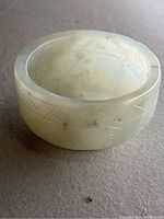 Image of small pale green translucent bowl with carved decorative leaf and abstract patterns on exterior side.