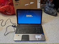 Open Toshiba laptop powered on showing startup screen, keyboard, and screen area.
