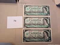 Photo showing three Canadian one dollar Centennial banknotes (1867-1967) with visible front face of each note featuring Queen Elizabeth II portrait.