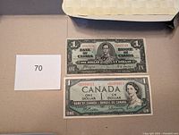 Both Canadian one dollar banknotes placed side by side with identification number 70 on the side; shows general condition and wear.
