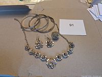 View of all items including three bracelets, necklace, earrings, and ring on cardboard surface.