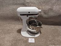 Front and side view of the KitchenAid Professional 300 stand mixer with stainless steel bowl and attachments inside the bowl on a textured surface.