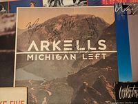 Close-up photo of the signed Arkells - Michigan Left album cover with mountains background and signatures visible.
