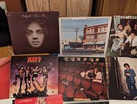 Photograph showing six vinyl records including Billy Joel albums, KISS Destroyer, and Loverboy albums with visible wear and some damage.