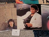 Close-up photo showing three records: George Harrison Somewhere In England, Michael Jackson Thriller, and an original soundtrack for Peter Gunn. Shows the condition and album cover visuals.