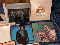 Close-up of Queen The Game, Queen A Night at the Opera, Cliff Richard I'm No Hero and Queen News of the World album covers laid on floor