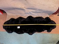 Full length of black sheepskin rug with tape measure showing approx 26 inch width