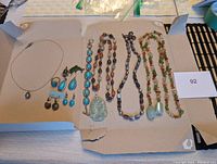 Wide shot of all jewelry included in the lot showing necklaces and earrings arranged on cardboard.