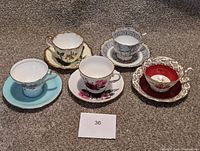 Front view of five teacup and saucer sets arranged in a line, showing varied floral patterns and color schemes.