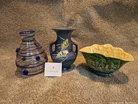 Front view of the blue glass vase, blue ceramic vase, and green ceramic bowl on beige carpet background.