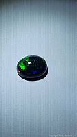 Oval cabochon-shaped Ethiopian AAA grade black opal displaying strong rolling flash in green and blue colors on a dark base, illuminated under focused light.
