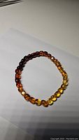 Photo of a round beaded bracelet made of polished Baltic amber beads, arranged in a gradient from dark to light yellow, placed on white paper.
