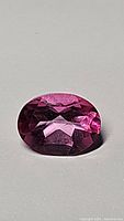 Close-up image of a natural hot pink oval cut topaz gemstone with visible facets and deep pink coloring on a neutral background.