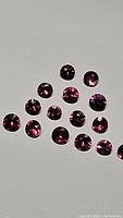 Photo of multiple round cut untreated ruby and sapphire gemstones, showing various sizes approximately 2.5-2.75mm, vibrant red and purple colors, high clarity.