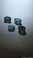 Four oval cut blue sapphires displayed on a textured surface under direct lighting, showing their color and cut.