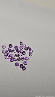 Group of small calibrated round amethyst gemstones on neutral background, showing rich purple color and good clarity.