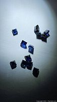 Loose square cut deep blue sapphires scattered on a white surface under bright light showing color and cut
