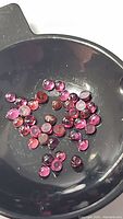 Photo showing group of small round polished cabochon Rhodolite garnet gemstones in dark container under natural light.