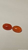 Two oval polished cabochon mandarin orange carnelian gemstones on plain light background, showing translucency and color.
