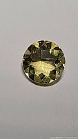 Single lemon citrine gemstone viewed from above showing its round fancy cut with deep golden yellow color and facets.