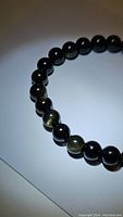Close-up photo showing the golden sheen effect on the round black obsidian beads of the bracelet.