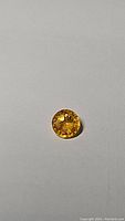 Close-up photo of a round cut golden yellow sapphire gemstone displaying good facets and clarity on white background.