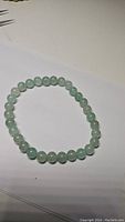 Photo showing round green aventurine gemstone bead bracelet stretched out against a white background.
