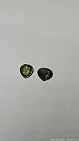 Two heart-shaped natural green sapphires on a plain background, showing color and cut details.